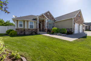 View of front facade featuring stone siding, roof with shingles, and concrete driveway
