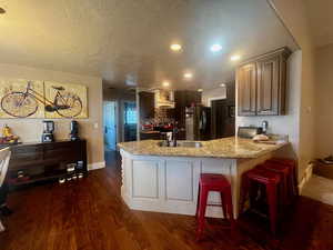Kitchen featuring a peninsula, a sink, a textured ceiling, and stainless steel refrigerator with ice dispenser