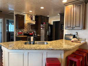 Kitchen with a peninsula, a textured ceiling, dark brown cabinets, appliances with stainless steel finishes, and a sink