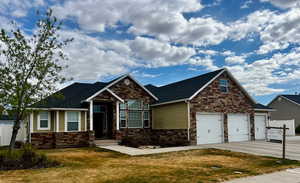 Craftsman inspired home with stone siding, an attached garage, a front lawn, and driveway