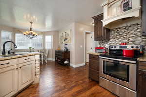 Kitchen with electric stove, a chandelier, dark brown cabinetry, decorative backsplash, and a textured ceiling
