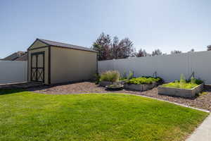 Fenced backyard featuring a vegetable garden and a storage unit