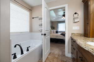 Ensuite bathroom featuring vanity, a bath, ceiling fan, and stone finish flooring