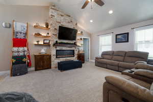 Carpeted living room featuring ceiling fan, vaulted ceiling, a stone fireplace, and recessed lighting
