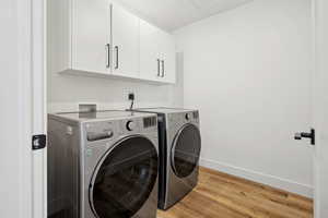 Laundry area with cabinet space, light wood finished floors, baseboards, and washer and clothes dryer