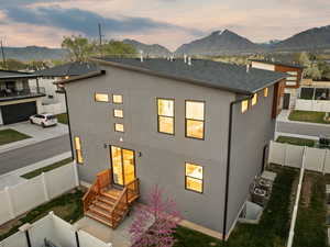 Back of house at dusk with a shingled roof, a fenced backyard, stucco siding, and a mountain view