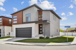 Contemporary house featuring a front lawn, driveway, fence, a garage, and stucco siding
