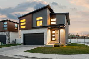 Contemporary home featuring concrete driveway, a lawn, stone siding, fence, and stucco siding