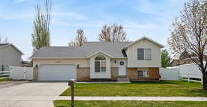 Tri-level home with a gate, fence, concrete driveway, an attached garage, and brick siding