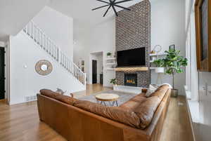 Living area featuring a towering ceiling, wood finished floors, visible vents, a fireplace, and ceiling fan