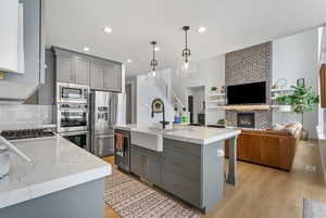 Kitchen with a sink, open floor plan, a brick fireplace, gray cabinetry, and appliances with stainless steel finishes