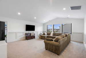 Living room with lofted ceiling, visible vents, light colored carpet, and a decorative wall