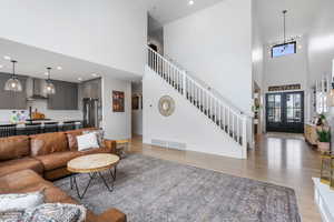 Living room featuring stairs, a towering ceiling, light wood finished floors, baseboards, and visible vents
