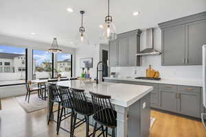 Kitchen with wall chimney range hood, gray cabinets, stainless steel gas cooktop, and a sink