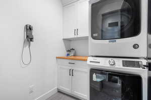 Laundry area with baseboards, cabinet space, stacked washer / drying machine, and light tile patterned floors
