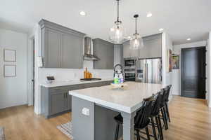 Kitchen with wall chimney exhaust hood, appliances with stainless steel finishes, gray cabinetry, and baseboards