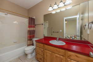Primary bathroom featuring tile patterned floors, toilet, shower / bath combo with shower curtain, a ceiling fan, and vanity
