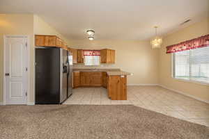 Kitchen featuring a chandelier, light countertops, a sink, a peninsula, and stainless steel refrigerator with ice dispenser