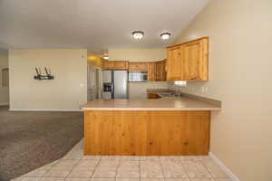 Kitchen featuring a sink, light tile patterned floors, light countertops, a peninsula, and appliances with stainless steel finishes