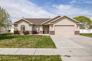 View of front of home with driveway, brick siding, a front yard, and a garage