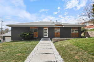 View of front of property with a shingled roof, a front yard, and stucco siding