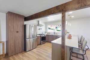 Kitchen with a sink, modern cabinets, light wood-style flooring, wall chimney exhaust hood, and appliances with stainless steel finishes