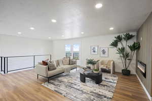 Living room with baseboards, wood finished floors, a textured ceiling, and recessed lighting