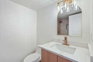 Bathroom featuring walk in shower, a textured ceiling, toilet, and vanity