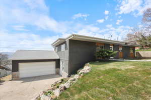 Mid-century inspired home featuring an attached garage, driveway, stone siding, and a front lawn