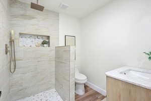 Full bathroom with a tile shower, wood finished floors, visible vents, toilet, and vanity