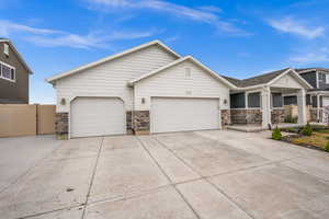 View of front of property featuring an attached garage, stone siding, concrete driveway, and fence