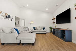 Living room with lofted ceiling, visible vents, and light wood finished floors