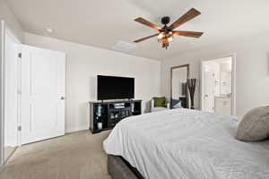 Carpeted bedroom with connected bathroom, ceiling fan, baseboards, and visible vents