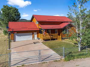 Chalet / cabin featuring a fenced front yard, concrete driveway, an attached garage, covered porch, and a front yard