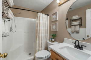 Bathroom with toilet, visible vents, vanity, and tiled shower