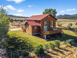 Back of house featuring a deck with mountain view, a lawn, a fenced backyard, and metal roof