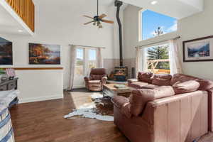 Living room with plenty of natural light, a towering ceiling, a wood stove, baseboards, and ceiling fan