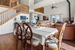 Dining area featuring wood finished floors, a wood stove, a towering ceiling, and ceiling fan