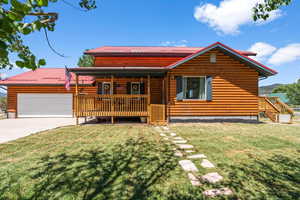 View of front facade with faux log siding, a front lawn, driveway, metal roof, and an attached garage