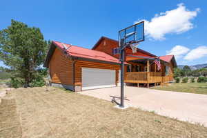 View of front facade with a front lawn, driveway, an attached garage, faux log siding, and metal roof