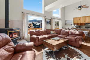Living area featuring ceiling fan, wood finished floors, a towering ceiling, and a wood stove