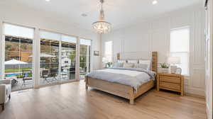 Bedroom featuring light wood-type flooring, a decorative wall, crown molding, a chandelier, and access to outside
