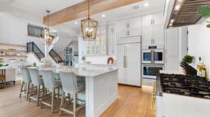 Kitchen featuring an inviting chandelier, exhaust hood, light wood-style floors, and paneled fridge