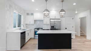 Kitchen featuring a sink, white cabinetry, custom range hood, a kitchen island, and appliances with stainless steel finishes