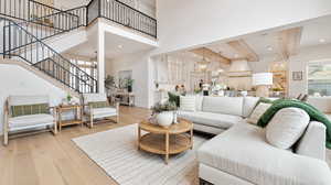 Living room with stairway, light wood finished floors, a towering ceiling, an inviting chandelier, and beamed ceiling