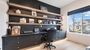 Home office with built in study area, baseboards, light wood finished floors, and visible vents