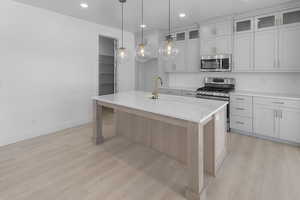 Kitchen with stainless steel appliances, light wood-style flooring, a sink, tasteful backsplash, and light countertops