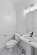Half bathroom featuring marble finish floor, toilet, and baseboards