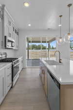 Kitchen with a wealth of natural light, a sink, appliances with stainless steel finishes, and a center island with sink