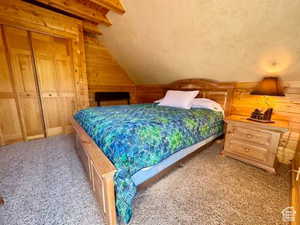 Bedroom with wood walls, carpet flooring, vaulted ceiling with beams, and a closet